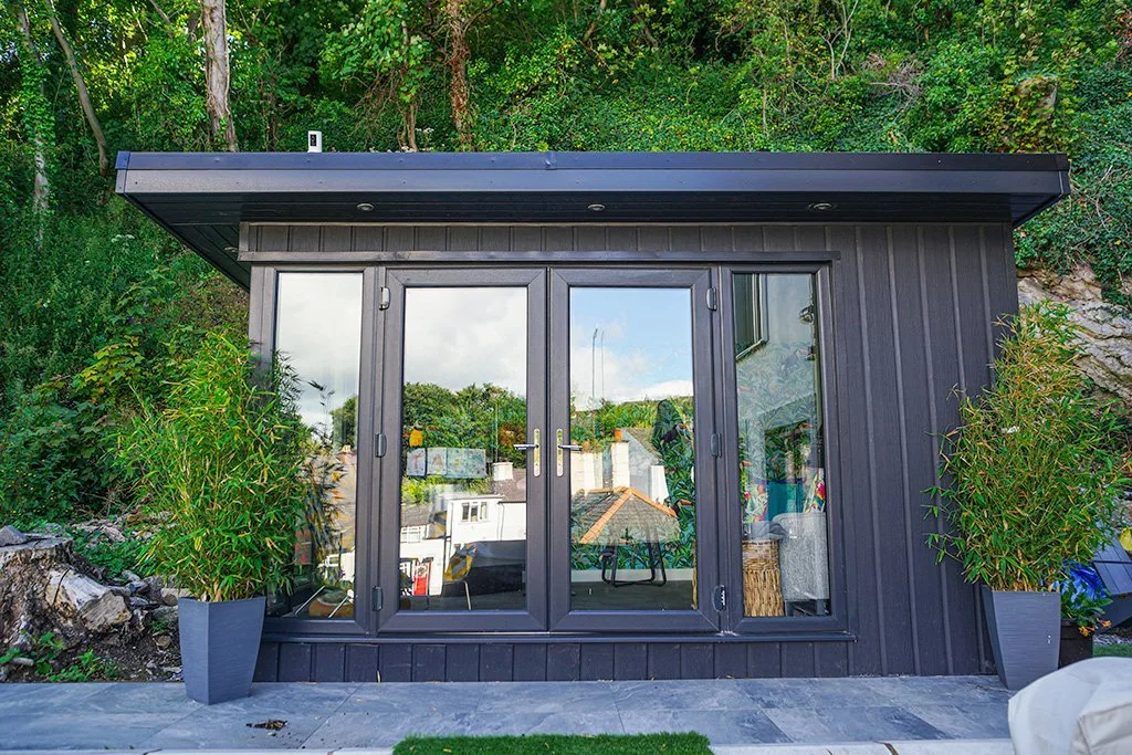 Dark-clad garden room with glazed doors in a planted garden