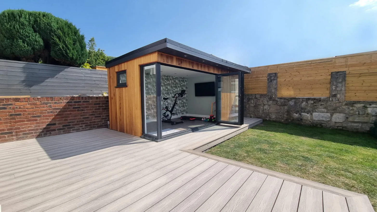 Timber-clad garden room with corner glazing opening onto a broad deck